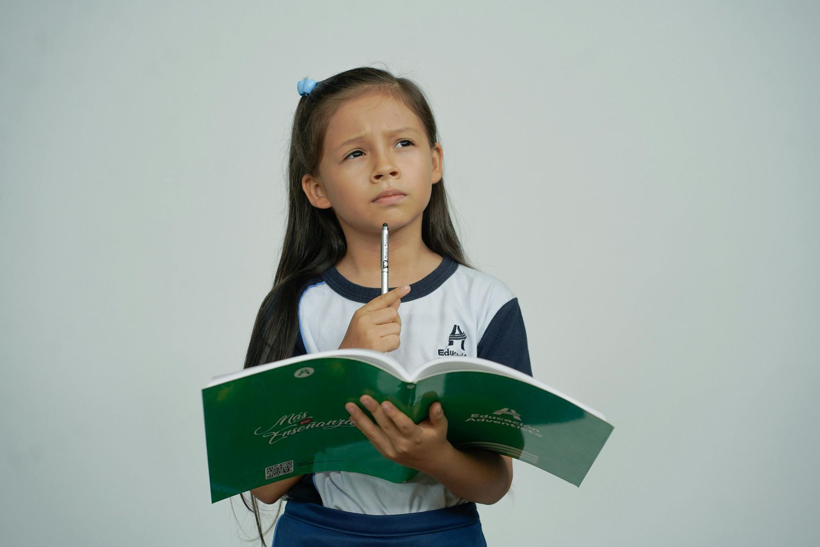 A girl holding an open book, pencil to her chin, wondering